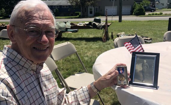 Mr John Dillon sitting at a table with a photo of his father SGT John T. Dillon and the Connecticut Service Medal.