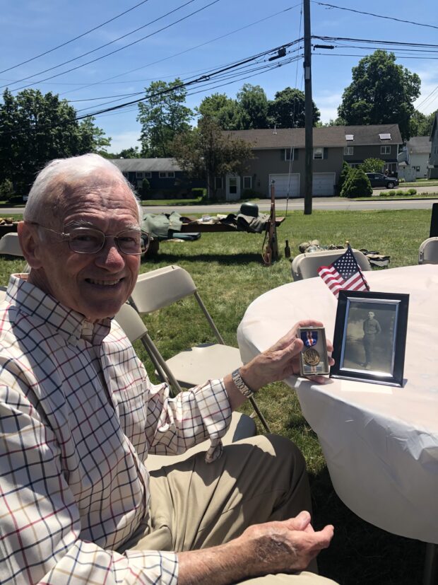 Mr. John Dillon Mr John Dillon sitting at a table with a photo of his father SGT John T. Dillon and the Connecticut Service Medal.